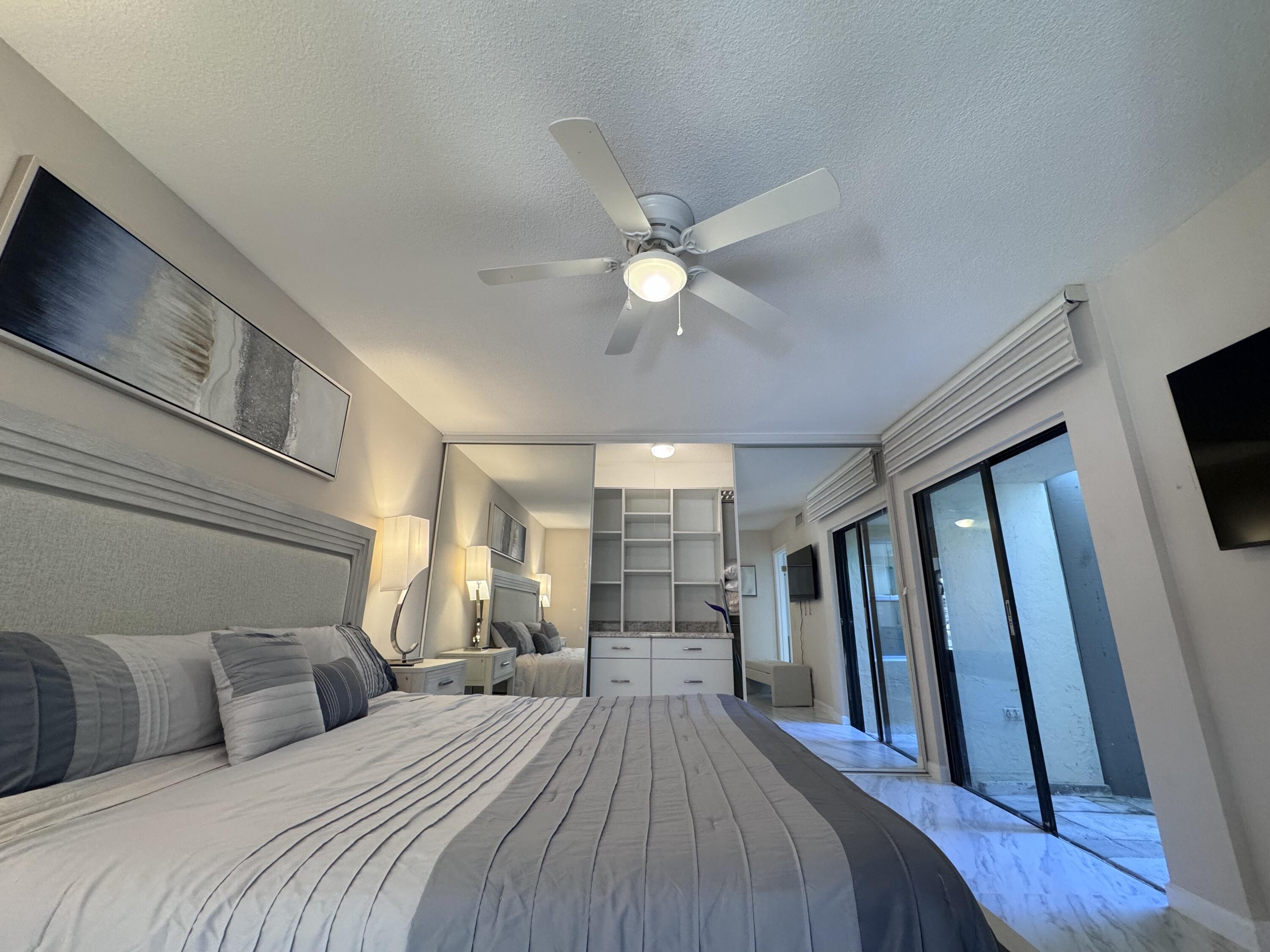 1605 Highway 1, Unit 1A Jupiter, FL 33477 - Photo 8 of 23 a bedroom with a large bed a flat tv screen and a ceiling fan