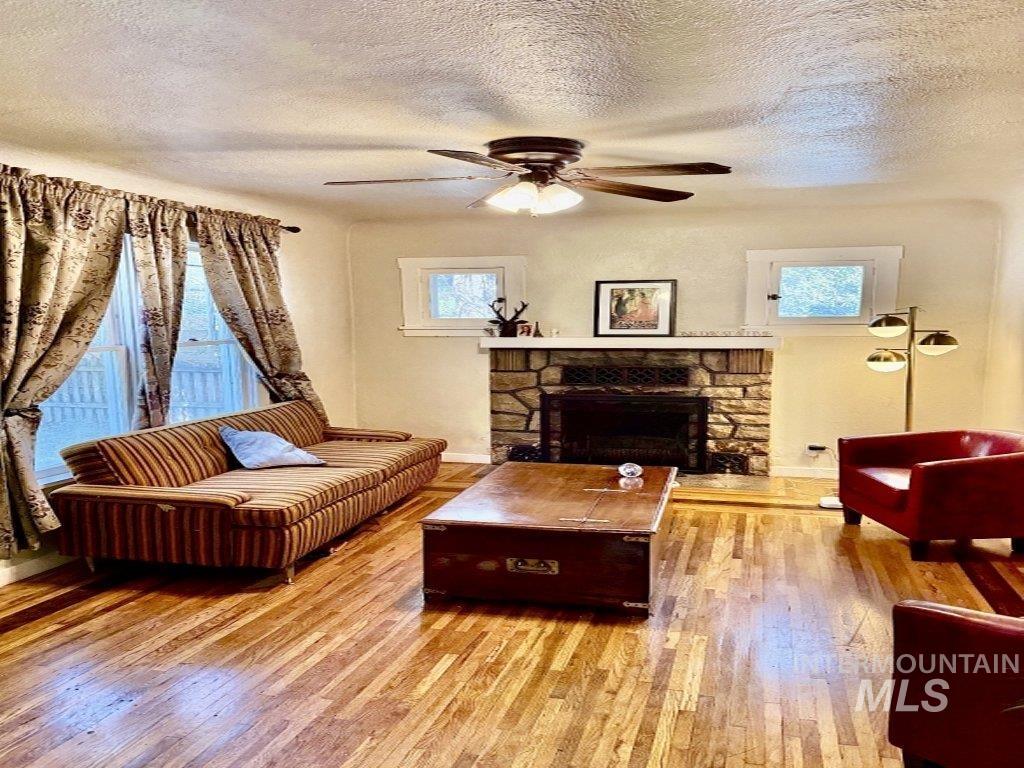 3605 West Morris Hill Road Boise, ID 83706 - Photo 2 of 3 Living area featuring wood-finish flooring, a stone fireplace with a hearth, white-framed windows, and a ceiling fan with integrated lighting
