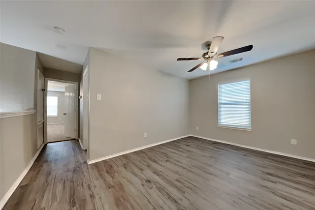 a view of an empty room with wooden floor and a ceiling fan