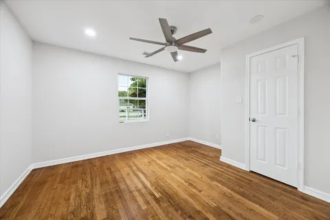 an empty room with wooden floor ceiling fan and windows