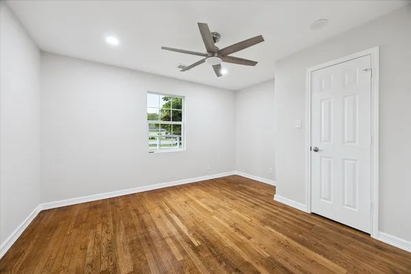 an empty room with wooden floor ceiling fan and windows