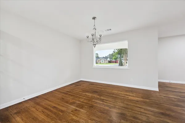 an empty room with wooden floor chandelier and windows