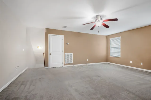 an empty room with chandelier fan and windows