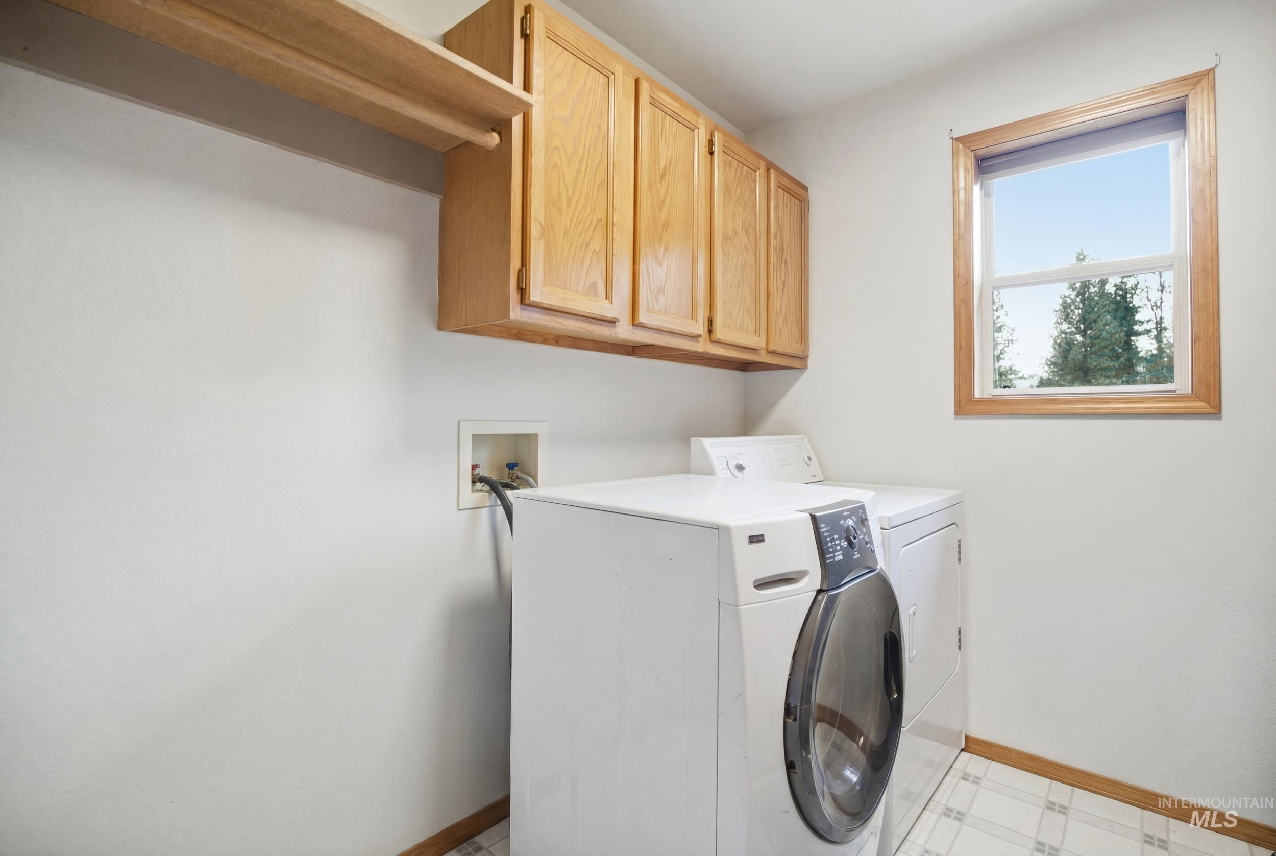 3980 North Pine-Featherville Road Mountain Home, ID 83647 - Photo 19 of 35 Laundry room with light wood-finish cabinetry, a window with wood trim, and patterned tile flooring