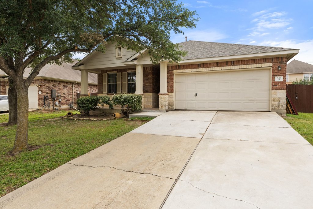 347 Spring Drive Kyle, TX 78640 - Photo 2 of 40 A classic brick exterior home with an attached garage, showcasing a manicured front yard and mature tree.