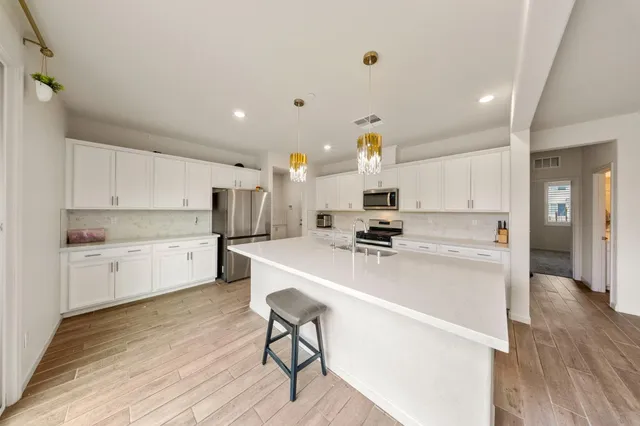 a large white kitchen with wooden floor and stainless steel appliances