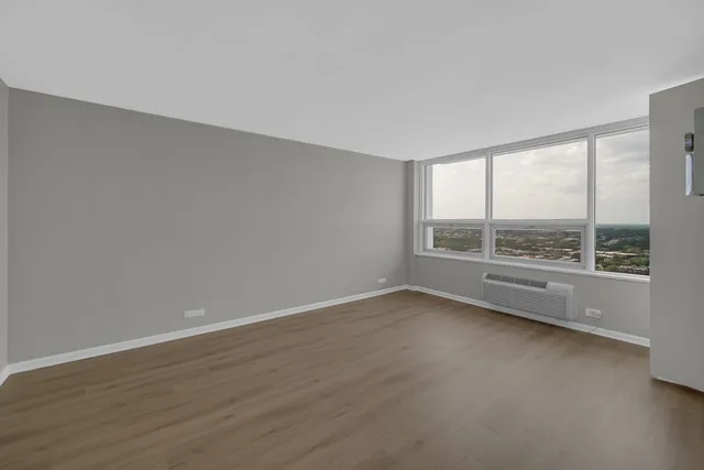 a view of an empty room with wooden floor and a window