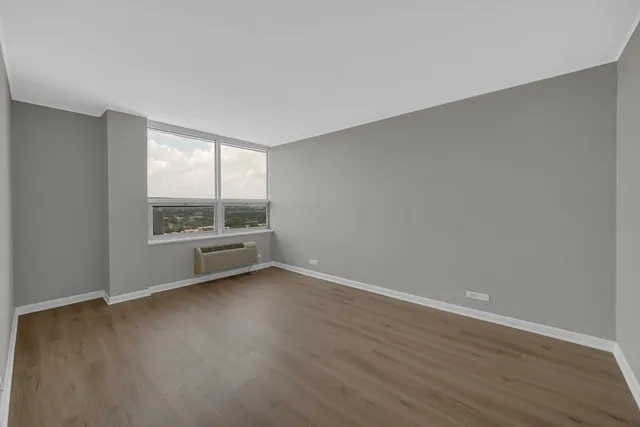 a view of an empty room with wooden floor and a window