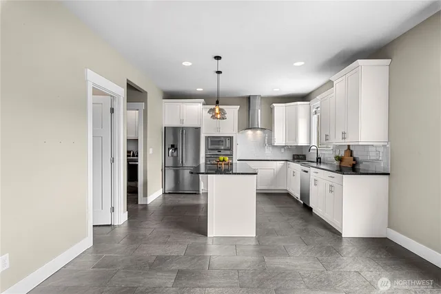 a kitchen with stainless steel appliances kitchen island granite countertop a sink and dishwasher a refrigerator with white cabinets