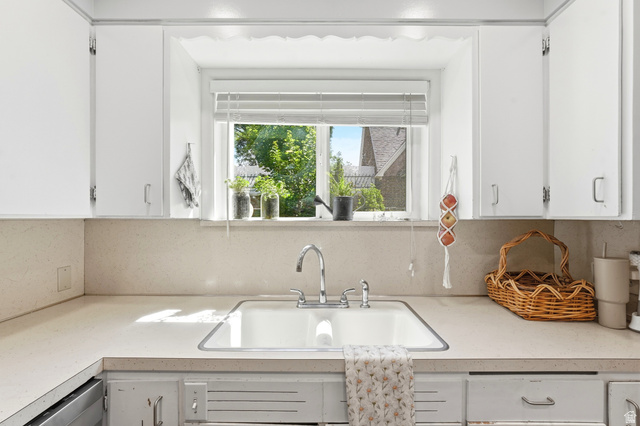 210 North 200 West Logan, UT 84321 - Photo 9 of 31 Kitchen area featuring white cabinetry, a single basin sink with a chrome faucet, light-toned countertops, and a window with horizontal blinds