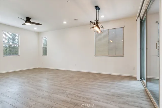 an empty room with wooden floor ceiling fan and windows