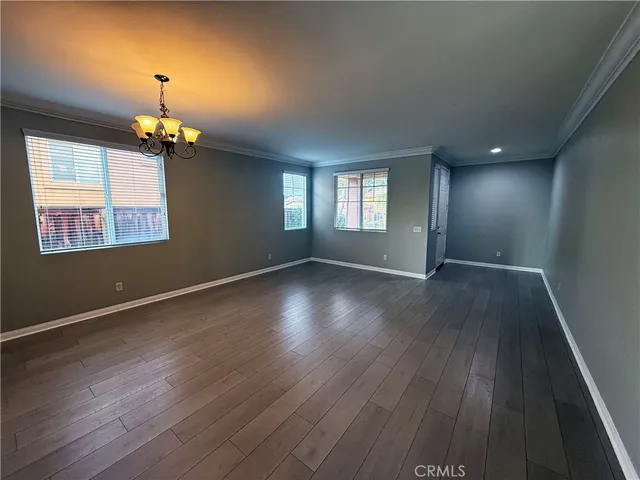 an empty room with wooden floor chandelier and windows
