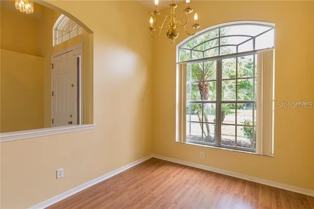 an empty room with wooden floor chandelier and windows