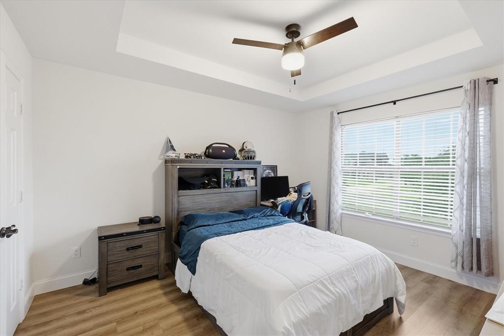 430 Ridgecrest Place Sanger, TX 76266 - Photo 21 of 40 Spacious room featuring a tray ceiling with a ceiling fan, a large window with horizontal blinds, and wood-finish flooring