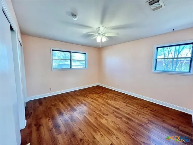 an empty room with wooden floor chandelier fan and windows