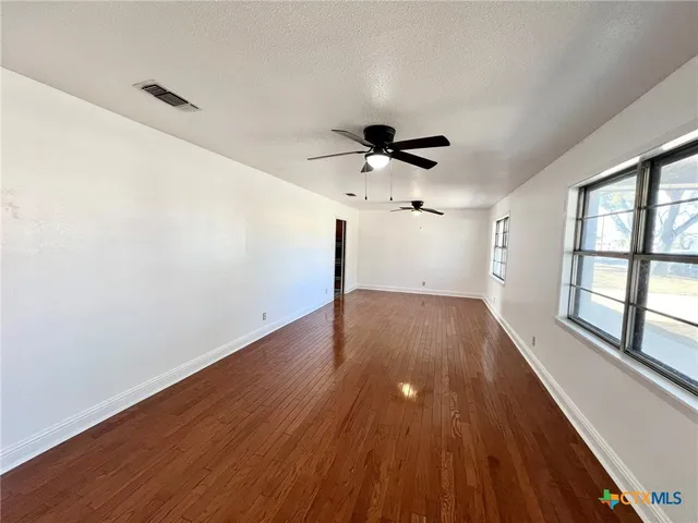 a view of empty room with wooden floor and fan