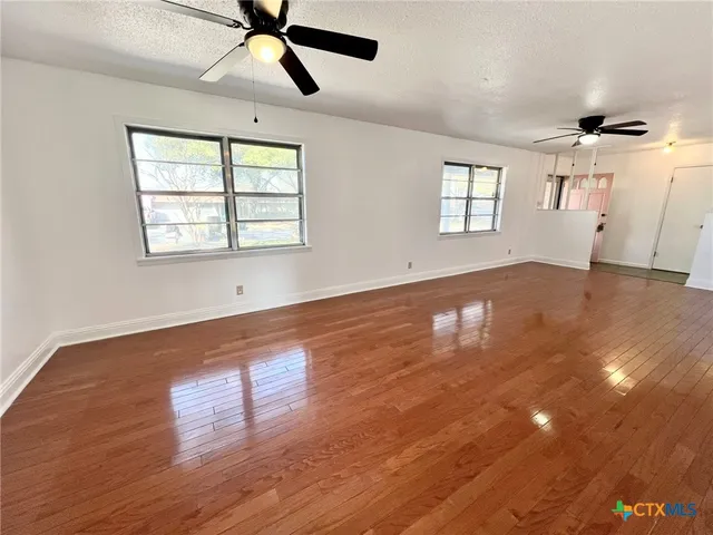 a view of empty room with wooden floor and fan