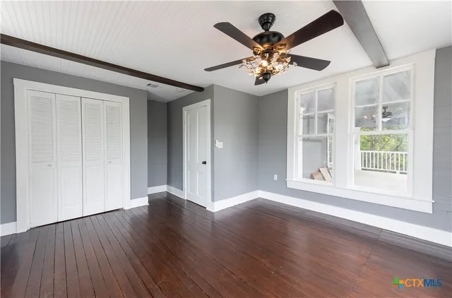a view of an empty room with wooden floor and a ceiling fan