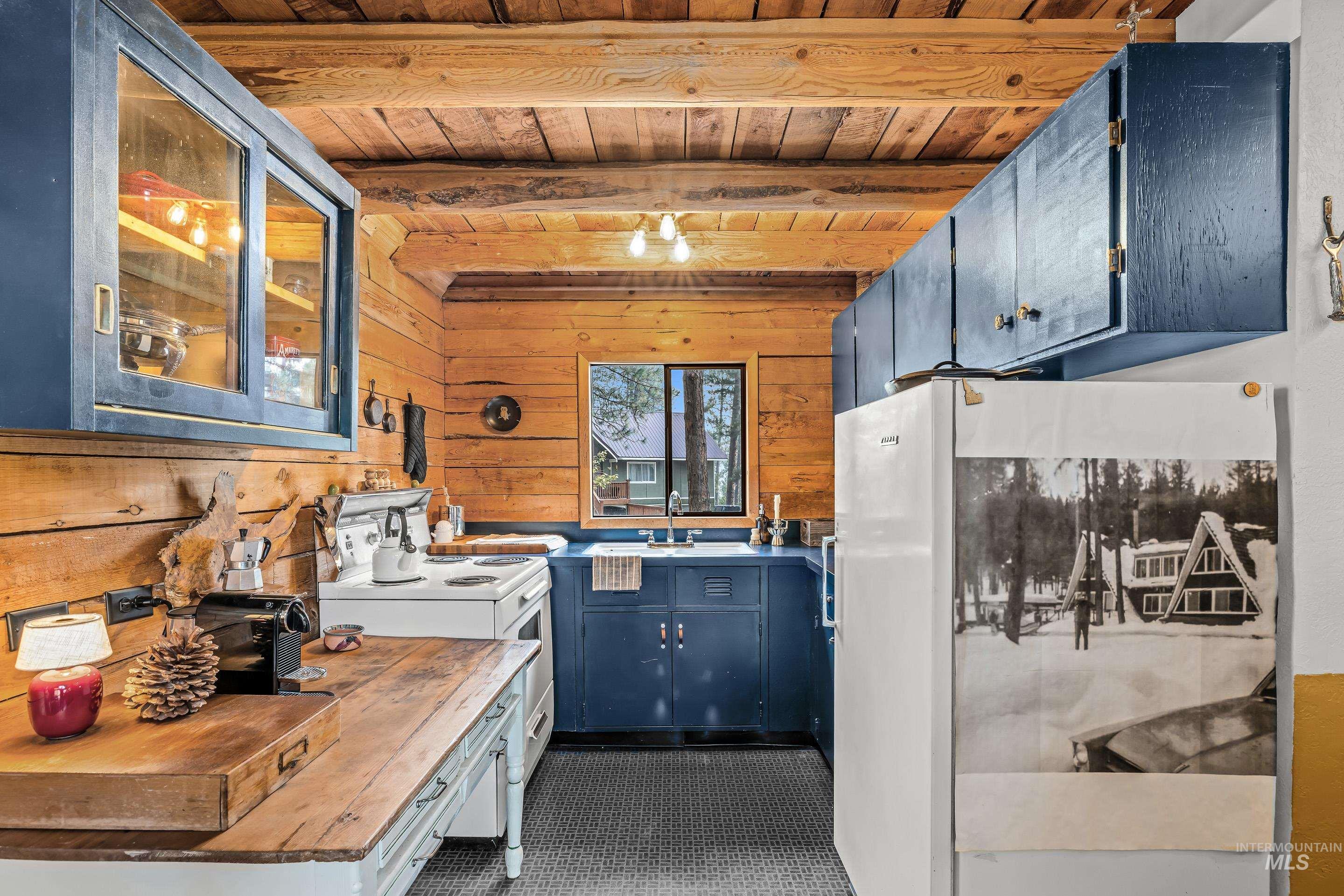 73 Rainbow Ridge Road Garden Valley, ID 83622 - Photo 10 of 49 Wood-paneled walls and ceiling, blue cabinetry, window with exterior view, white built-in appliances, and wood countertops