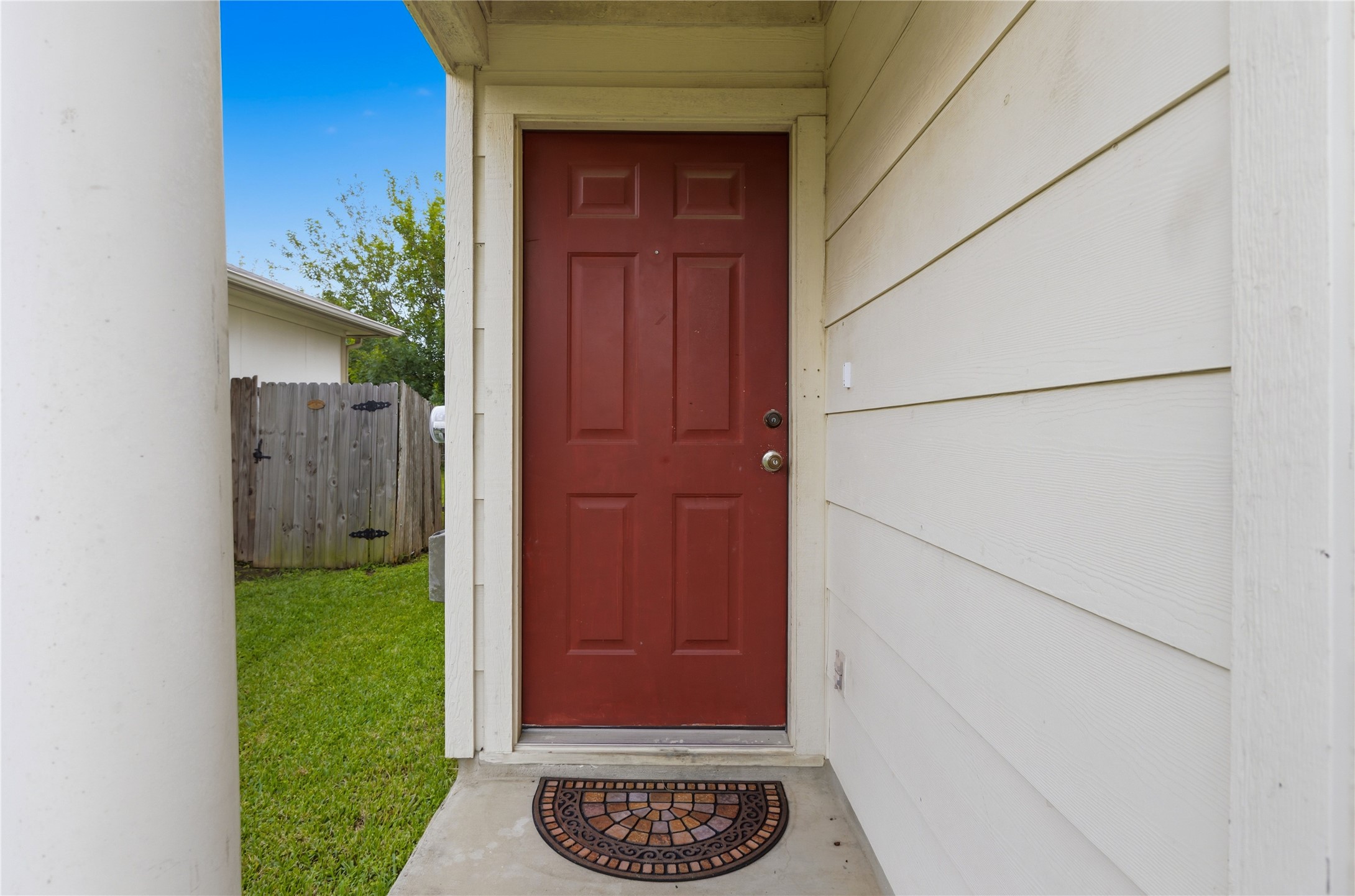 16112 Hamilton Point Circle Manor, TX 78653 - Photo 3 of 27 Red paneled entry door with round knob hardware, concrete entryway, horizontal plank siding, and a partial view of a wooden fence