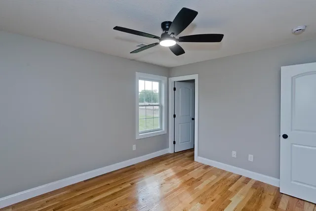 a view of an empty room with wooden floor and a ceiling fan