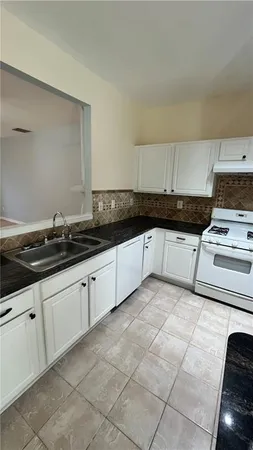 a large kitchen with granite countertop a stove a sink a counter space and cabinets