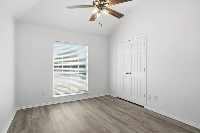 an empty room with wooden floor fan and windows