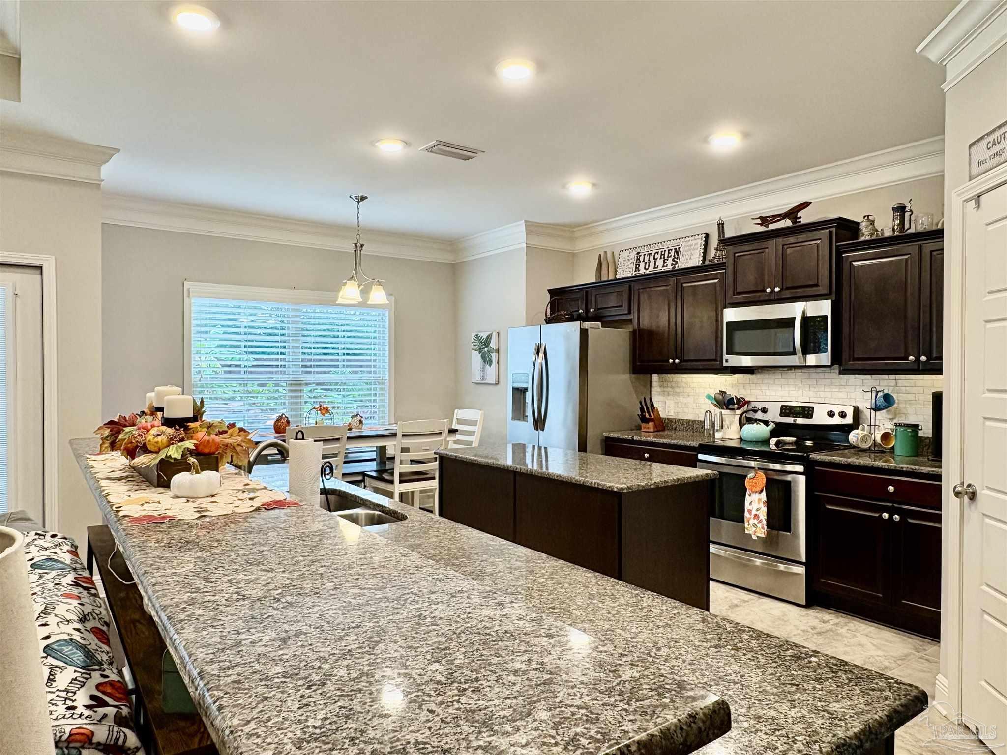 1700 Kahuna Way Cantonment, FL 32533 - Photo 14 of 34 a kitchen with stainless steel appliances kitchen island granite countertop a refrigerator oven a sink dishwasher a dining table and chairs with wooden floor