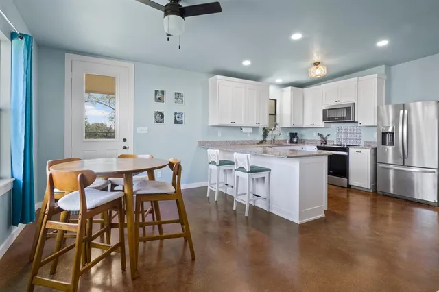 a kitchen with stainless steel appliances kitchen island granite countertop a dining table chairs refrigerator sink and cabinets