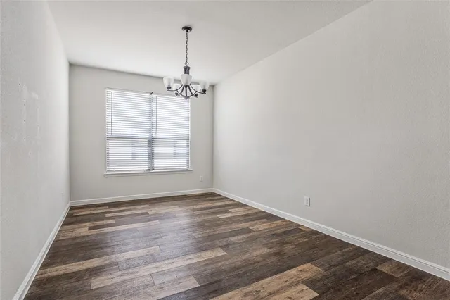 an empty room with wooden floor chandelier and windows