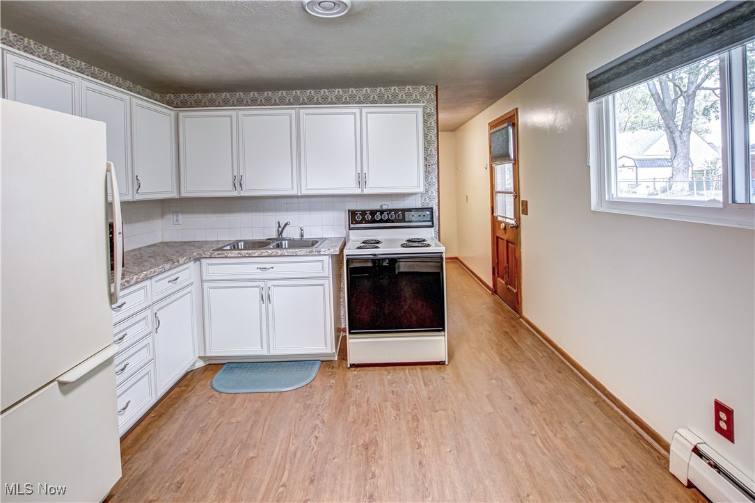 706 Abbe Road South Elyria, OH 44035 - Photo 10 of 34 Kitchen with white appliances, light countertops, light wood-type laminate flooring, white cabinets, and baseboard heating