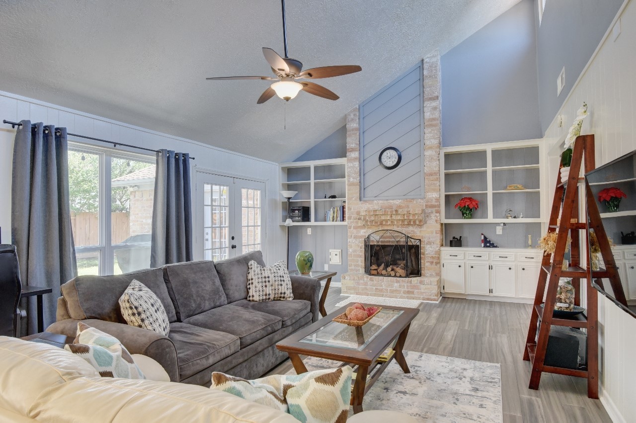 25810 Fairbrook Lane Spring, TX 77373 - Photo 6 of 33 This inviting living room features a high vaulted ceiling with a ceiling fan, a cozy brick fireplace, and built-in shelving. Large windows and glass doors let in plenty of natural light, while the neutral color palette and modern furnishings create a comfortable and stylish space.