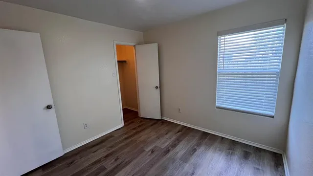 a view of an empty room with wooden floor and a window