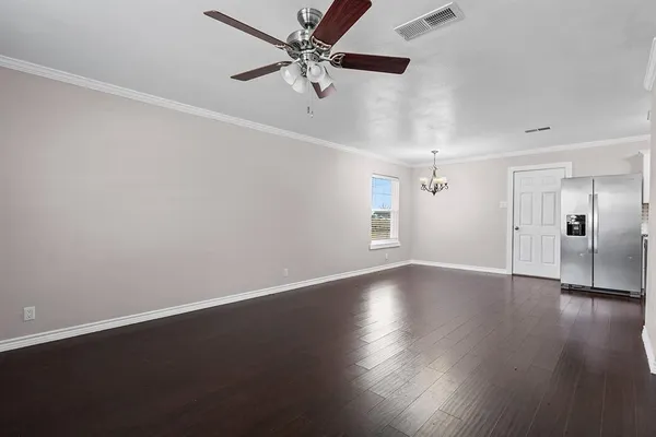 an empty room with wooden floor chandelier fan and windows