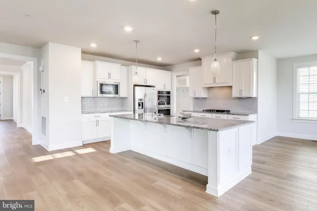 a kitchen with kitchen island granite countertop a sink a stove a refrigerator and white cabinets