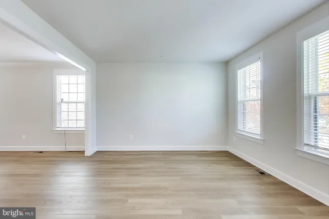 an empty room with wooden floor and windows with curtains
