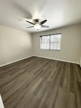 an empty room with wooden floor fan and windows