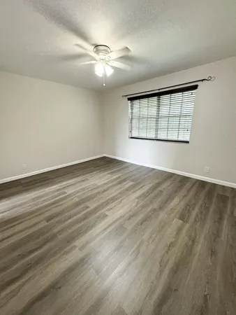 an empty room with wooden floor chandelier fan and windows