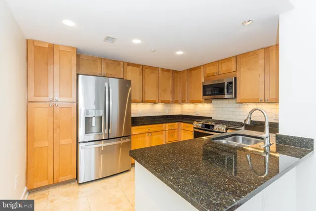 a kitchen with granite countertop a refrigerator a sink a stove top oven a counter space and cabinets