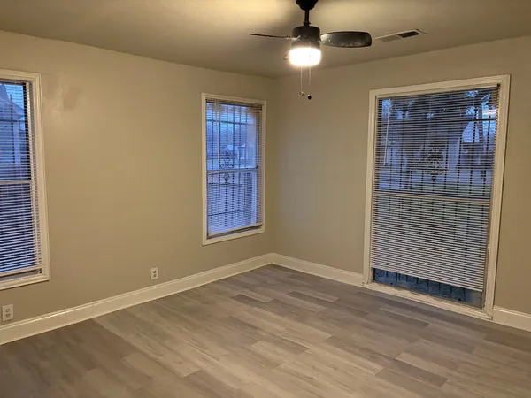 an empty room with wooden floor fan and windows