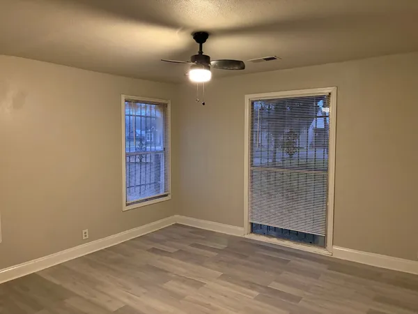 an empty room with wooden floor fan and windows