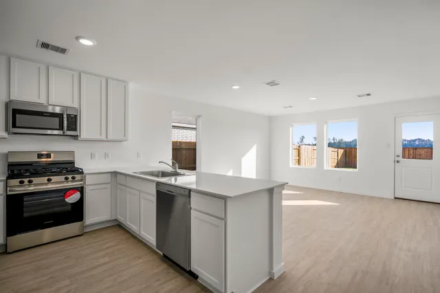 a kitchen with stainless steel appliances granite countertop a stove top oven a sink dishwasher and a refrigerator with wooden floor