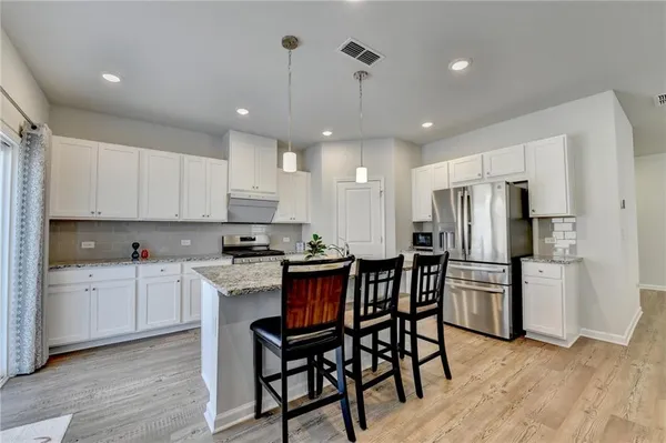 a kitchen with stainless steel appliances granite countertop a dining table chairs refrigerator and microwave
