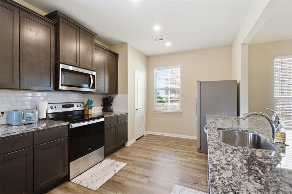 292 Wandering Stream Way Princeton, TX 75407 - Photo 13 of 40 Modern kitchen featuring dark wood cabinetry, stainless steel appliances, speckled countertops, and wood-finish flooring