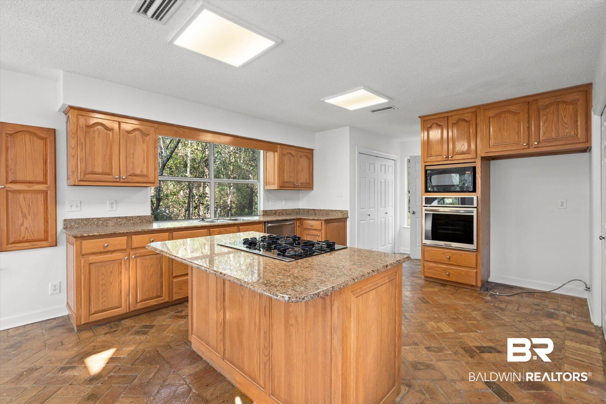 3847 Riviere Du Chien Road Mobile, AL 36693 - Photo 14 of 51 Kitchen with wood finish cabinets, light stone countertops, black appliances, a center island, and brick flooring