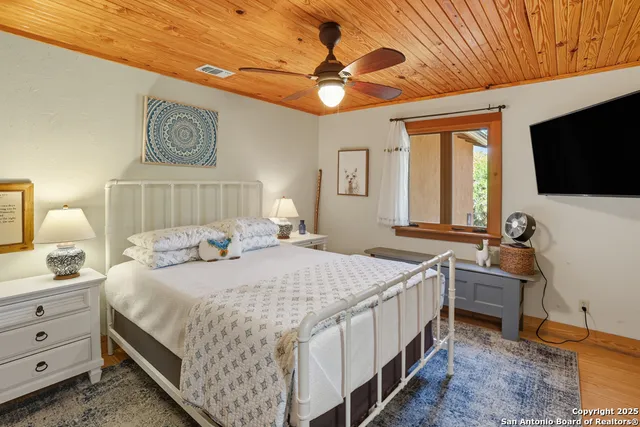 a bedroom with a bed a chandelier and a flat tv screen on the dresser