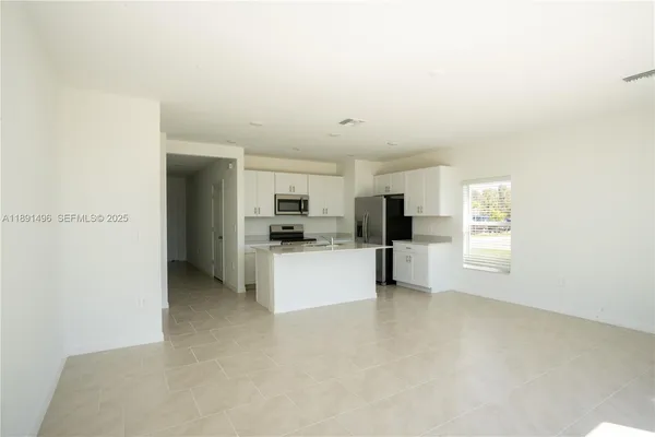 a view of kitchen with stainless steel appliances kitchen island refrigerator stove and white cabinets