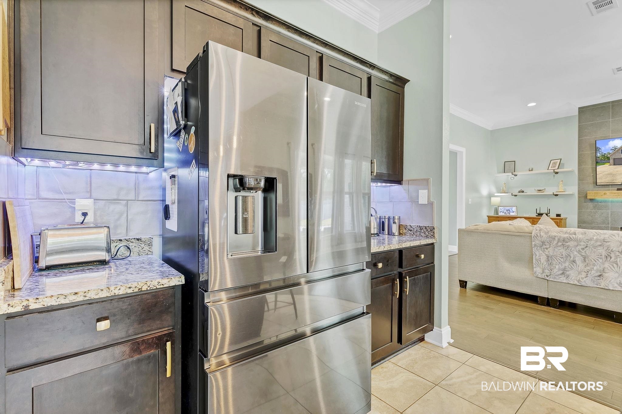 30635 Drayton Court Daphne, AL 36527 - Photo 18 of 51 Kitchen with stainless steel fridge with ice dispenser, ornamental molding, dark brown cabinets, tasteful backsplash, and light stone countertops
