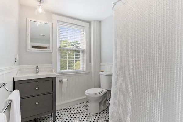 a bathroom with a toilet a sink a mirror a window and vanity