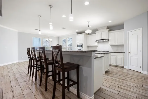 a kitchen with stainless steel appliances kitchen island granite countertop a table chairs and white cabinets